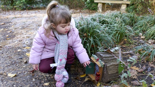 Small girl opening a fairy door in the garden at Mottisfont